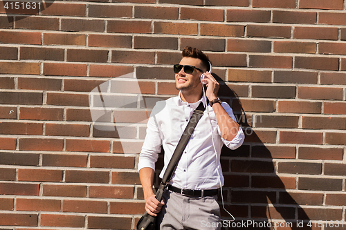 Image of young man in headphones with bag over brickwall