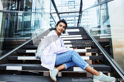 Image of young cute modern indian girl at university building sitting on stairs reading a book, wearing hipster glasses, lifestyle people concept