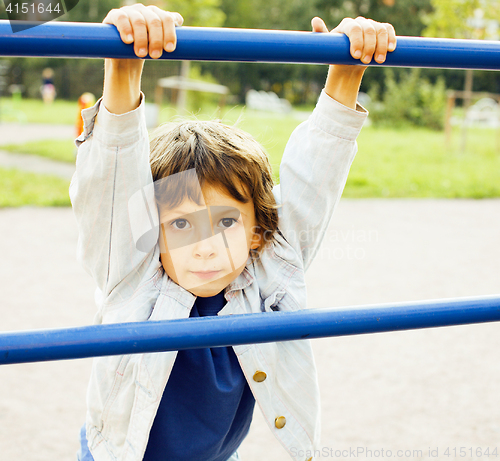 Image of little cute boy playing on playground, hanging on gymnastic ring