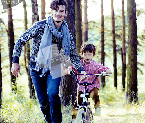 Image of father learning his son to ride on bicycle outside in green park, lifestyle people concept