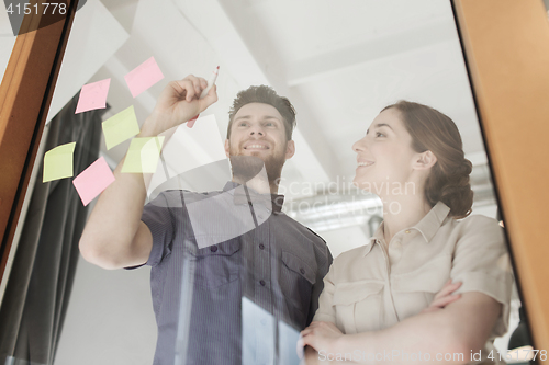 Image of happy creative team writing on blank office glass