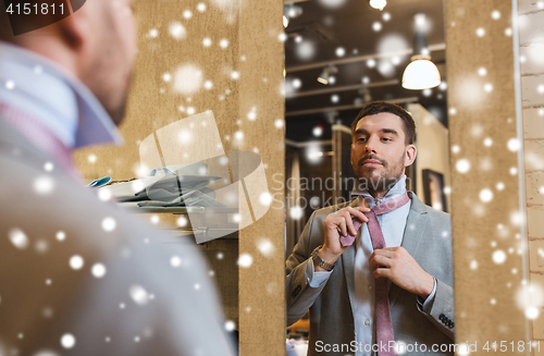 Image of man tying tie on at mirror in clothing store