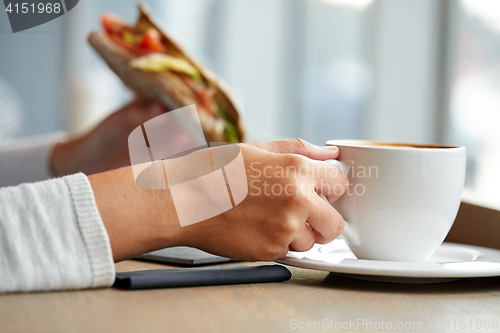 Image of woman drinking coffee and eating sandwich at cafe