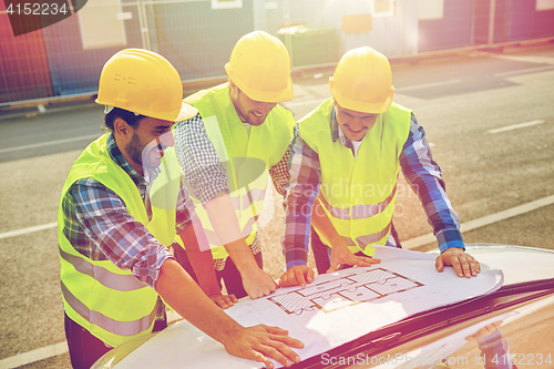 Image of close up of builders with blueprint on car hood