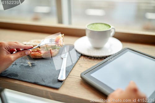 Image of woman with tablet pc and panini sandwich at cafe