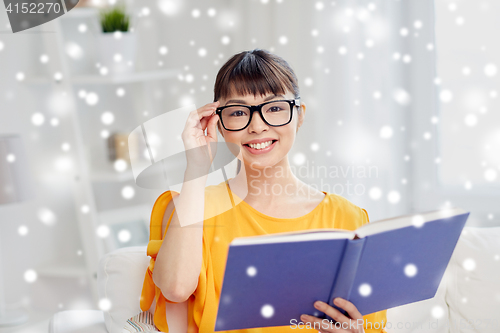 Image of smiling young asian woman reading book at home