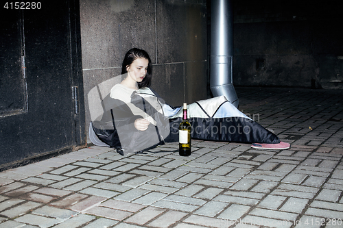 Image of young poor ttenage girl sitting at dirty wall on floor with bottle of vine, poor refugee alcoholic, hopeless homeless woman in depression, real junky concept