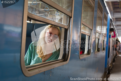 Image of Blonde caucasian woman riding a train, looking trough window.