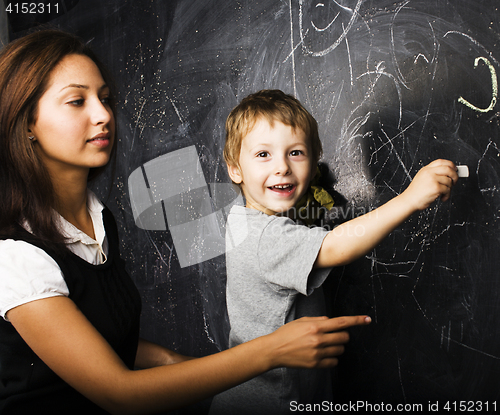 Image of little cute boy with young teacher in classroom studying at blackboard smiling, lifestyle people concept