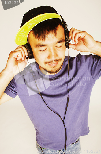 Image of young asian man in hat and headphones listening music on white b