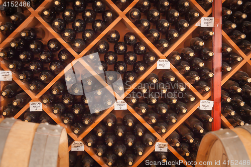 Image of Several Varietal Wine Bottles and Barrels Age Inside Cellar