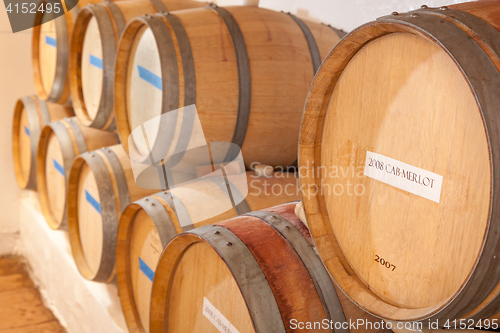 Image of Wine Barrels and Bottles Age Inside Dark Cellar.