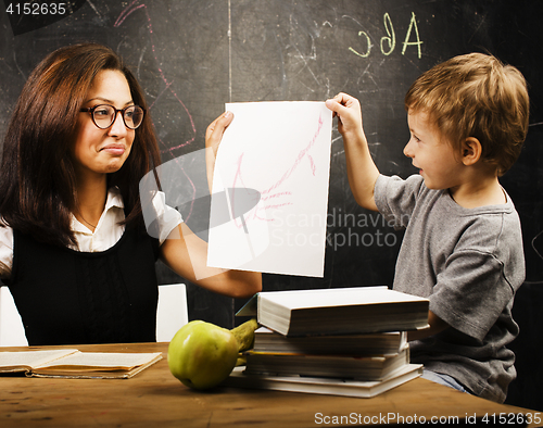 Image of little cute boy with young teacher in classroom studying at blackboard smiling, lifestyle people concept