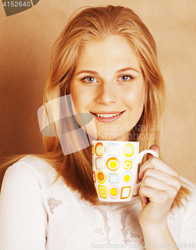 Image of young cute blond girl drinking coffee close up on warm brown bac