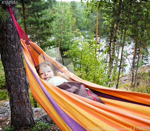 Image of little cute real boy in hammock smiling against landscape with forest and lake hight on mountain, lifestyle people concept