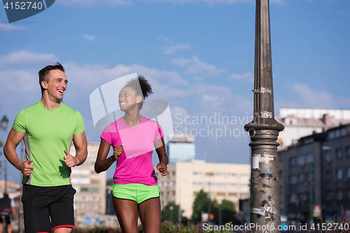 Image of young smiling multiethnic couple jogging in the city