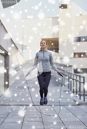 Image of happy woman exercising with jump-rope outdoors