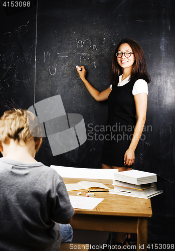 Image of little cute boy with young teacher in classroom studying at blac