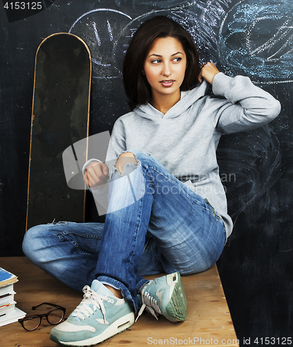 Image of young cute teenage girl in classroom at blackboard seating on ta