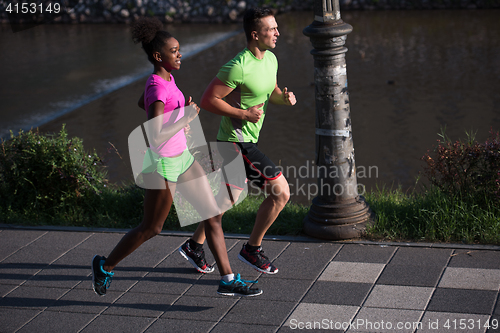 Image of young smiling multiethnic couple jogging in the city