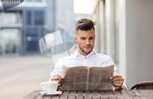 Image of smiling man reading newspaper at city street cafe