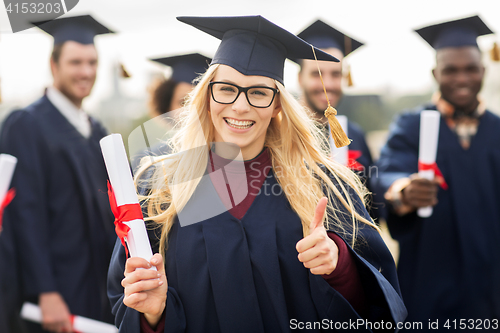 Image of happy students with diplomas showing thumbs up