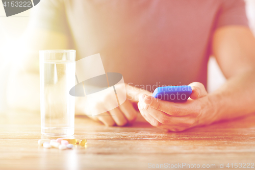 Image of close up of hands with smartphone, pills and water