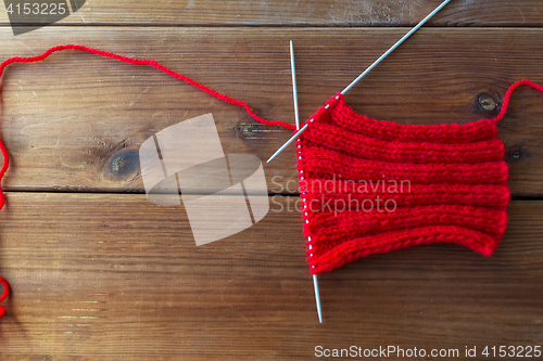 Image of hand-knitted item with knitting needles on wood