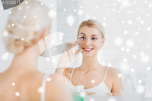 Image of woman with curler curling eyelashes at bathroom