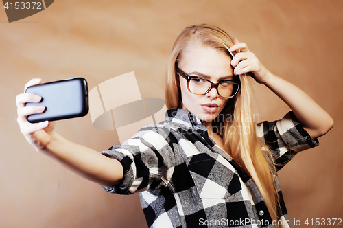 Image of young pretty blond hipster girl making selfie on warm brown back