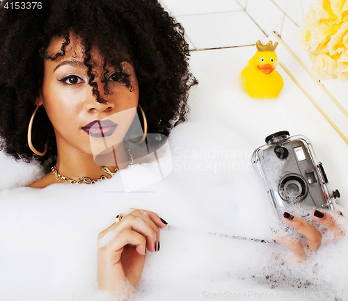 Image of young afro-american teen girl laying in bath with foam, wearing 