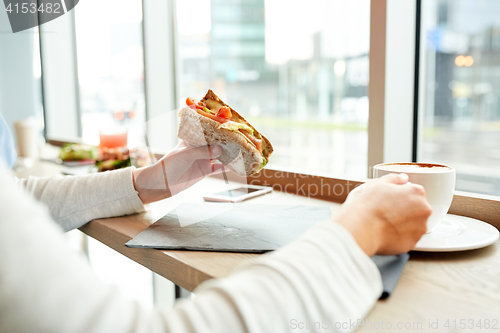 Image of woman eating sandwich and drinking coffee at cafe