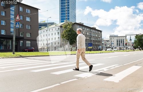 Image of senior man walking along city crosswalk