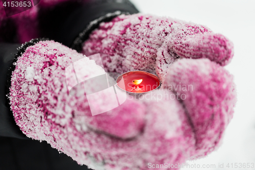 Image of close up of hands in winter mittens holding candle