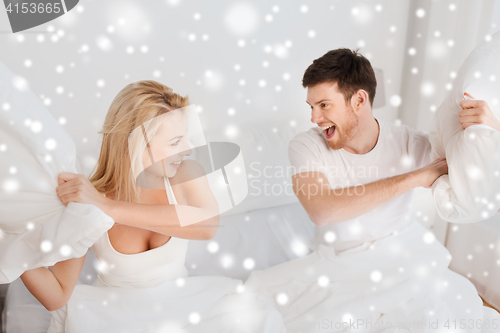 Image of happy couple having pillow fight in bed at home