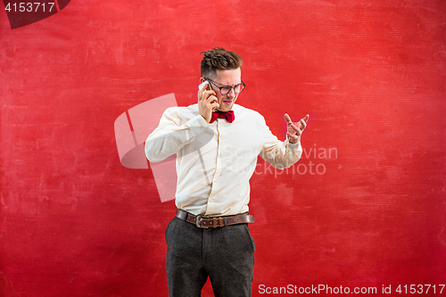 Image of Portrait of puzzled man talking by phone a red background