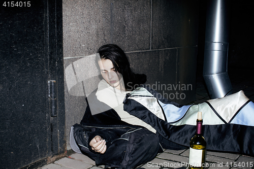 Image of young poor ttenage girl sitting at dirty wall on floor with bottle of vine, poor refugee alcoholic, hopeless homeless woman in depression, real junky concept