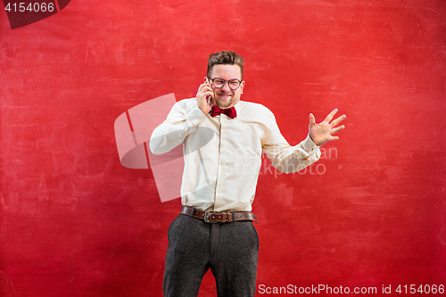 Image of Portrait of puzzled man talking by phone a red background