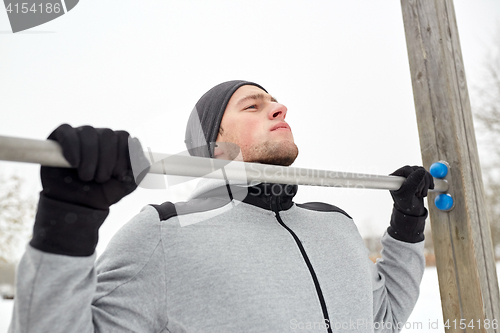 Image of young man exercising on horizontal bar in winter