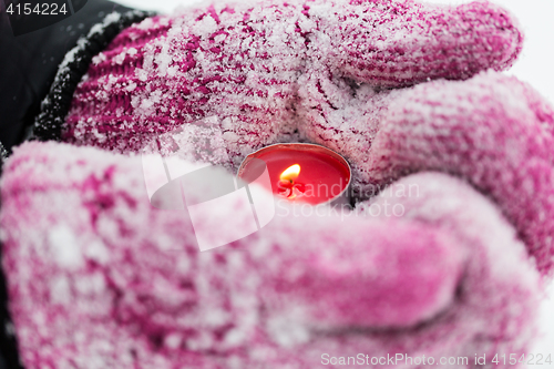 Image of close up of hands in winter mittens holding candle