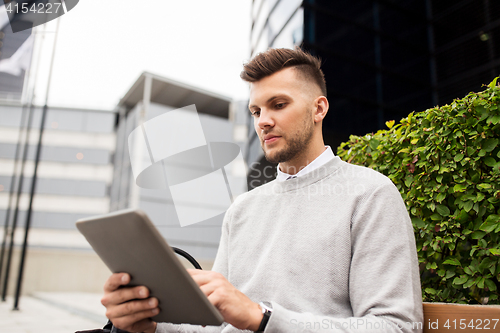 Image of man with tablet pc sitting on city street bench