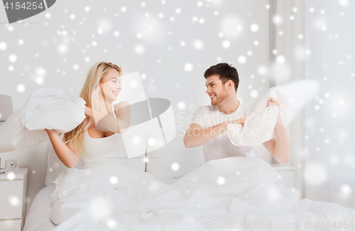 Image of happy couple having pillow fight in bed at home