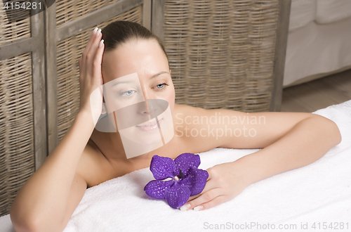 Image of stock photo attractive lady getting spa treatment in salon, healthcare people concept, woman with purple flower orchid dreaming on white towel