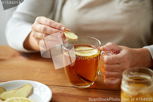 Image of close up of woman adding ginger to tea with lemon