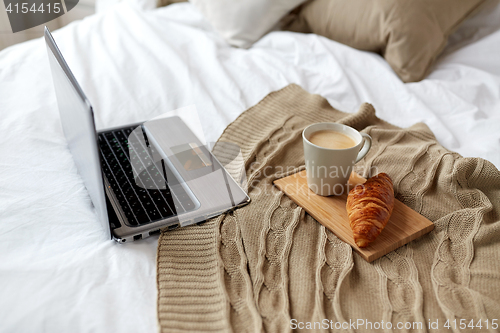 Image of laptop, coffee and croissant on bed at cozy home