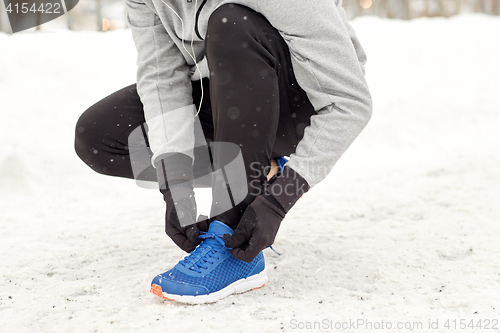 Image of man with earphones tying sports shoes in winter