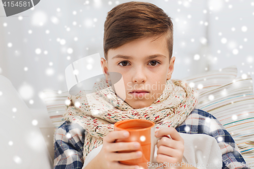 Image of ill boy with flu in scarf drinking tea at home