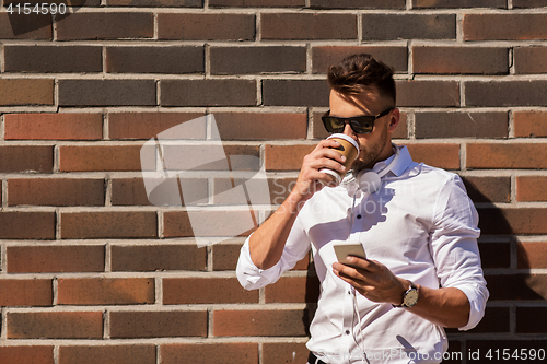 Image of man with smartphone and coffee cup on city street