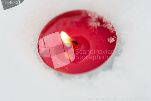 Image of burning christmas candle on snow in winter