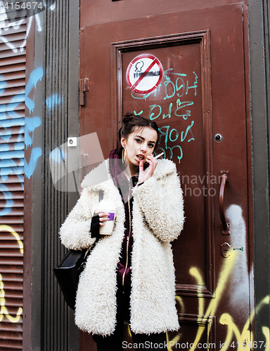 Image of young pretty stylish teenage girl outside at city wall with graf